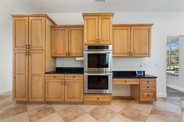 kitchen with dark countertops, stainless steel double oven, baseboards, and light tile patterned floors