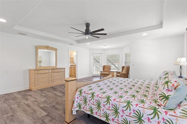 bedroom with a tray ceiling, baseboards, visible vents, and wood finished floors