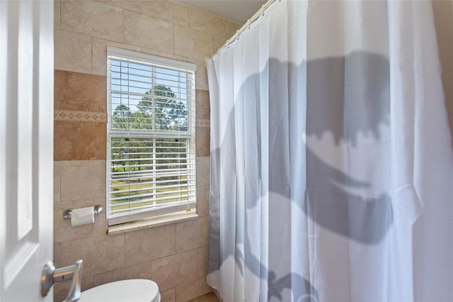 full bath featuring a shower with curtain, tile walls, toilet, and a healthy amount of sunlight