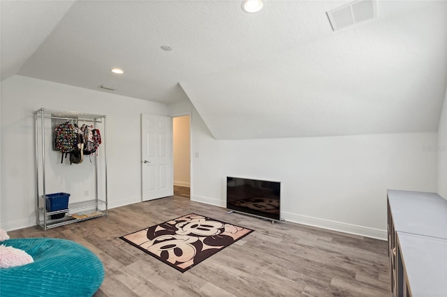 interior space with visible vents, baseboards, wood finished floors, and vaulted ceiling