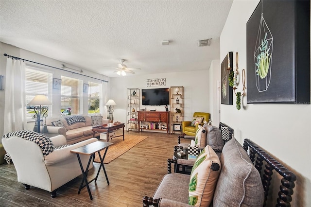 living room with a textured ceiling, wood finished floors, visible vents, and ceiling fan