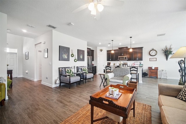 living area featuring a ceiling fan, baseboards, visible vents, dark wood finished floors, and a textured ceiling