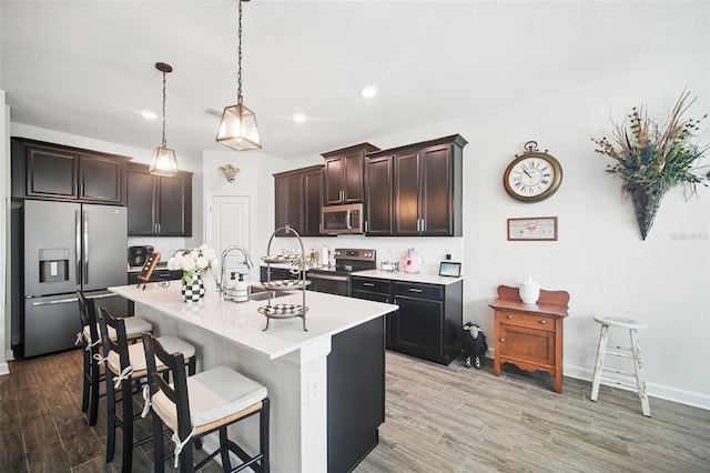 kitchen featuring light wood-style flooring, appliances with stainless steel finishes, light countertops, and a kitchen breakfast bar