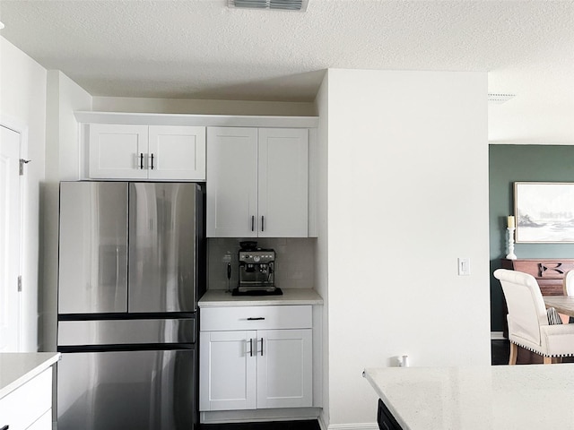 kitchen featuring visible vents, white cabinetry, tasteful backsplash, and freestanding refrigerator