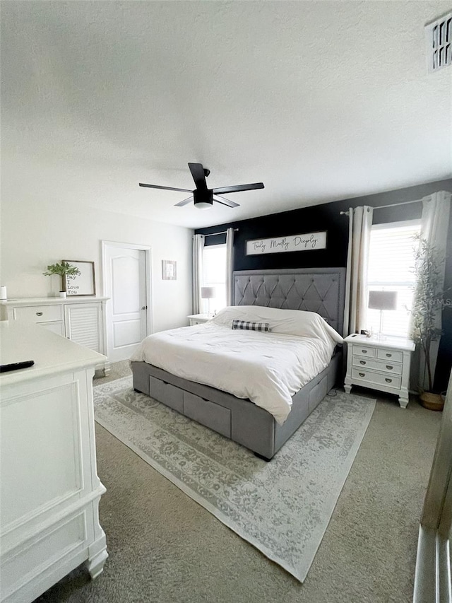 carpeted bedroom featuring a ceiling fan, visible vents, and a textured ceiling