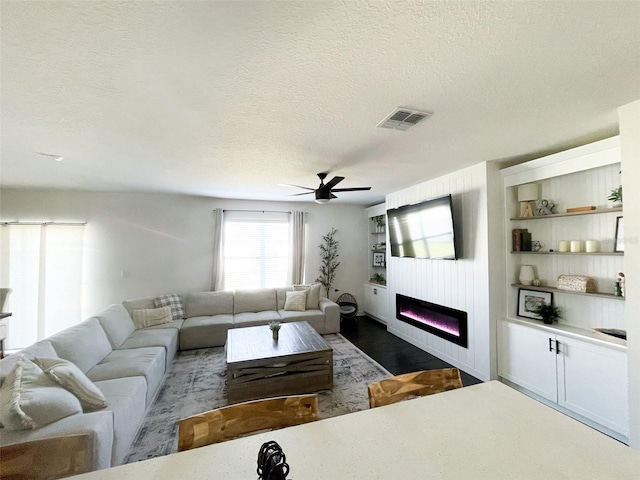 living area featuring a glass covered fireplace, a ceiling fan, visible vents, and a textured ceiling