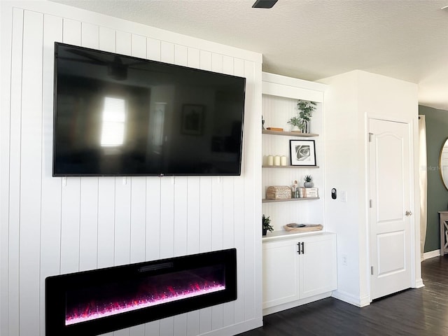 details featuring a glass covered fireplace, a textured ceiling, baseboards, and wood finished floors