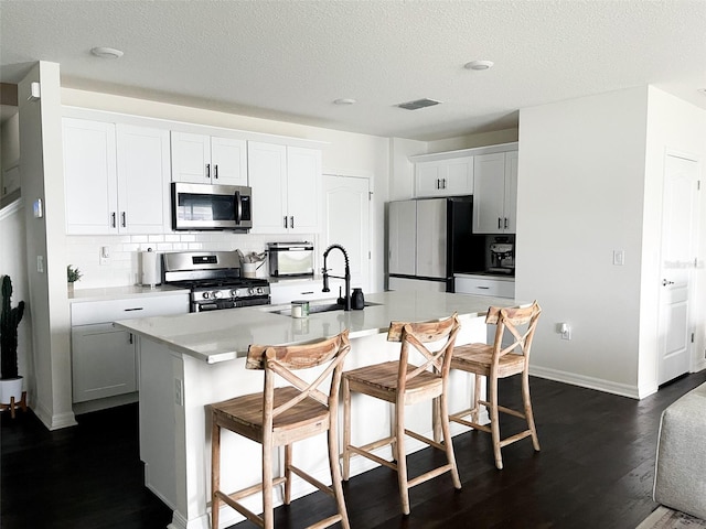 kitchen featuring visible vents, a sink, backsplash, appliances with stainless steel finishes, and a breakfast bar area