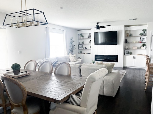 dining space with visible vents, built in shelves, a textured ceiling, dark wood-style floors, and a glass covered fireplace