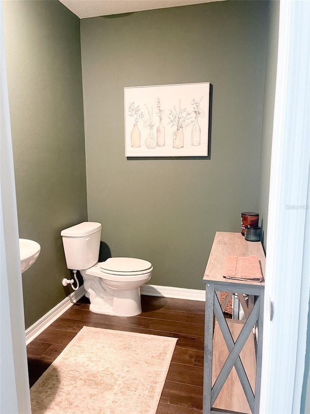 half bath with toilet, wood finished floors, and baseboards