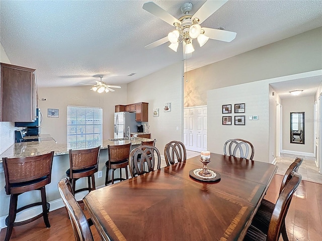 dining space with light wood finished floors, plenty of natural light, ceiling fan, vaulted ceiling, and a textured ceiling