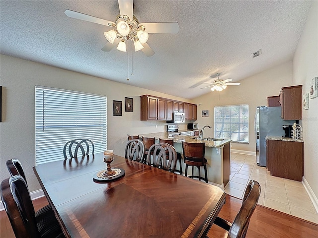 dining room with light tile patterned floors, visible vents, lofted ceiling, ceiling fan, and a textured ceiling