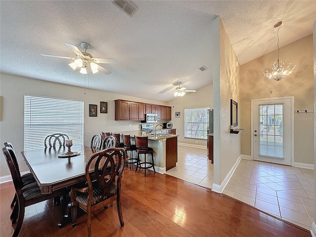 dining space with a wealth of natural light, light wood-style flooring, vaulted ceiling, and ceiling fan with notable chandelier