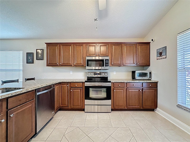 kitchen with a sink, a textured ceiling, light stone counters, and stainless steel appliances