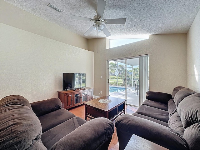 living room featuring visible vents, lofted ceiling, a ceiling fan, and a textured wall