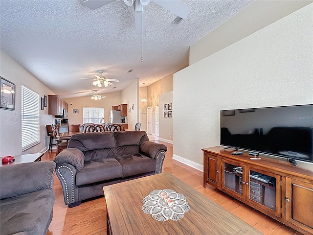 living room with a textured ceiling, vaulted ceiling, light wood-style floors, and ceiling fan