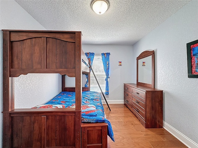 bedroom featuring baseboards, a textured wall, light wood-type flooring, and a textured ceiling