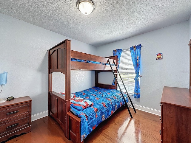 bedroom with a textured wall, baseboards, and wood finished floors