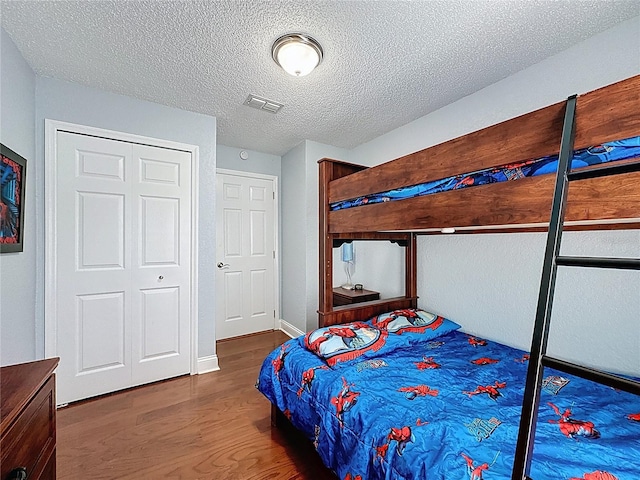 bedroom featuring visible vents, a textured ceiling, baseboards, and wood finished floors