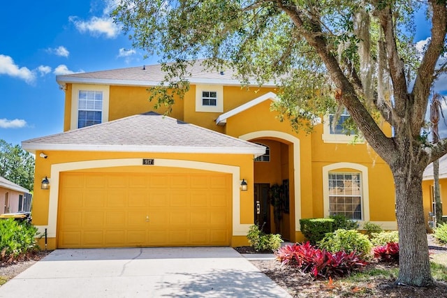 traditional-style house featuring stucco siding, driveway, a shingled roof, and a garage