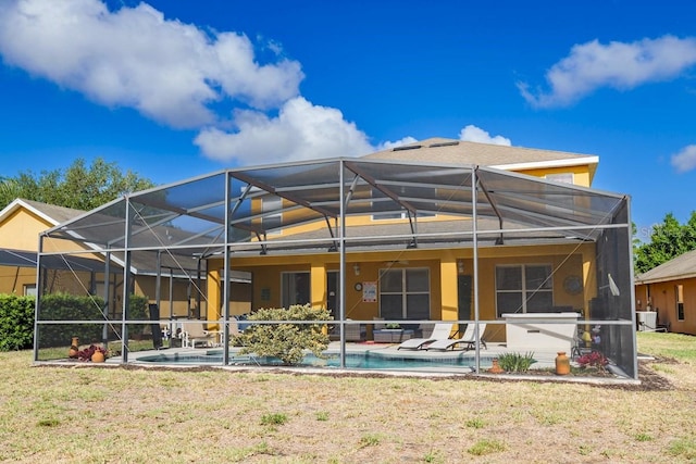 rear view of property featuring glass enclosure, a patio, an outdoor pool, stucco siding, and a lawn