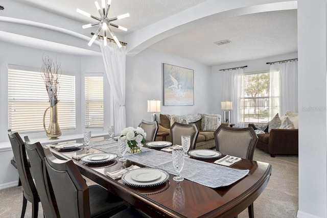 dining area with visible vents, light carpet, an inviting chandelier, arched walkways, and a textured ceiling