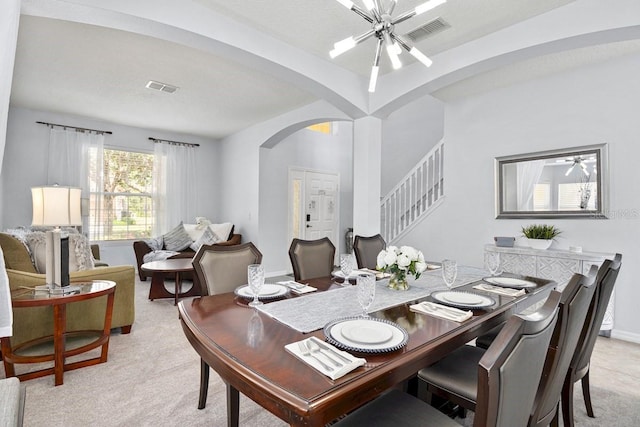 dining room with arched walkways, visible vents, stairway, and light carpet