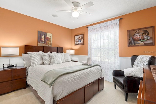 bedroom featuring light carpet, wainscoting, and a ceiling fan