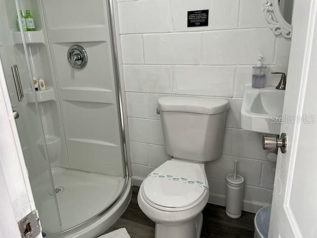 bathroom featuring a stall shower, toilet, tile walls, and wood finished floors