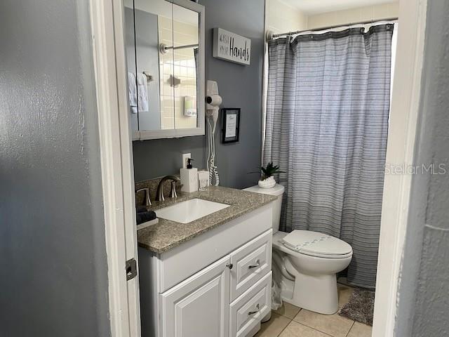 bathroom featuring tile patterned flooring, a shower with shower curtain, toilet, and vanity