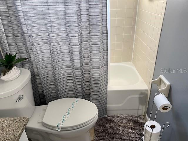 full bath featuring toilet and shower / tub combo with curtain