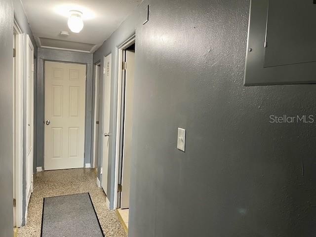 hallway with electric panel, speckled floor, and a textured wall