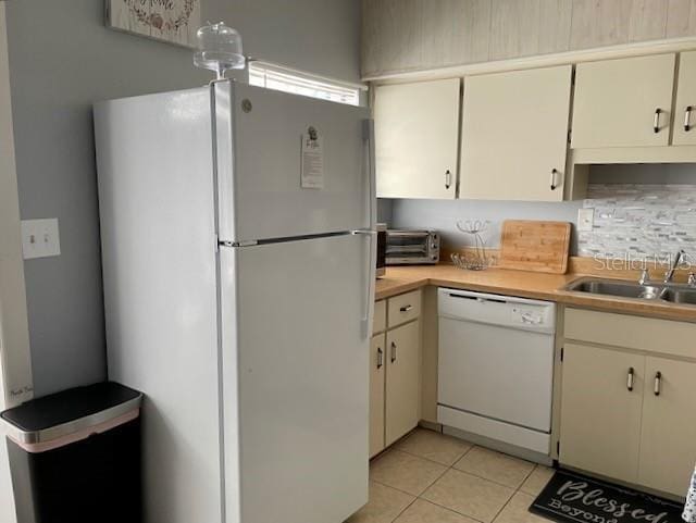 kitchen with backsplash, light countertops, light tile patterned floors, white appliances, and a sink