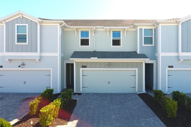 multi unit property featuring decorative driveway, board and batten siding, an attached garage, and a shingled roof