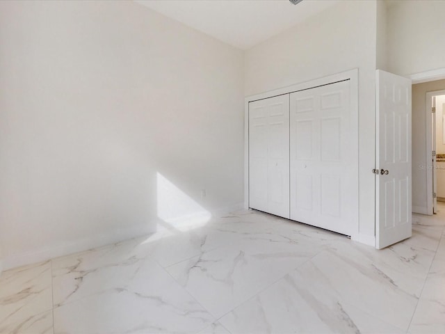 unfurnished bedroom featuring baseboards, marble finish floor, and a closet