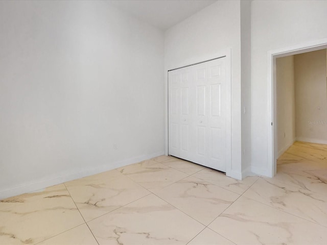 unfurnished bedroom with baseboards, marble finish floor, and a closet