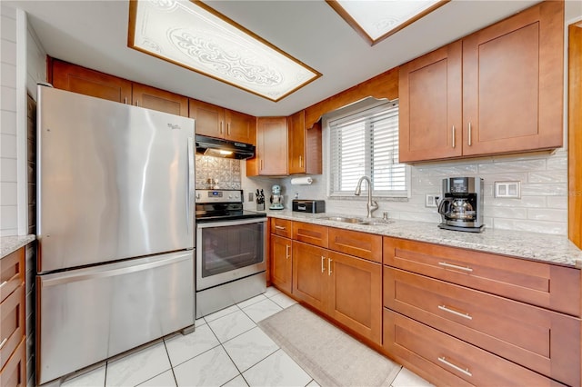 kitchen with a sink, brown cabinetry, under cabinet range hood, and stainless steel appliances