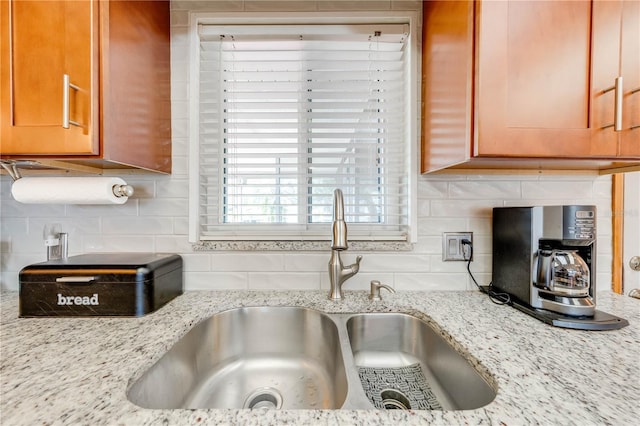 kitchen featuring light stone counters, backsplash, and a sink