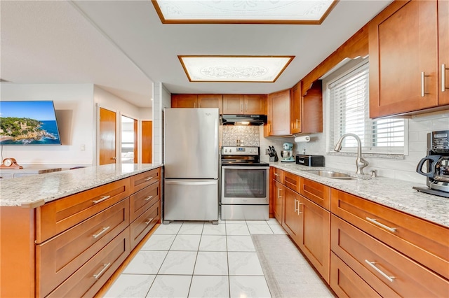 kitchen featuring under cabinet range hood, a sink, appliances with stainless steel finishes, brown cabinetry, and light stone countertops