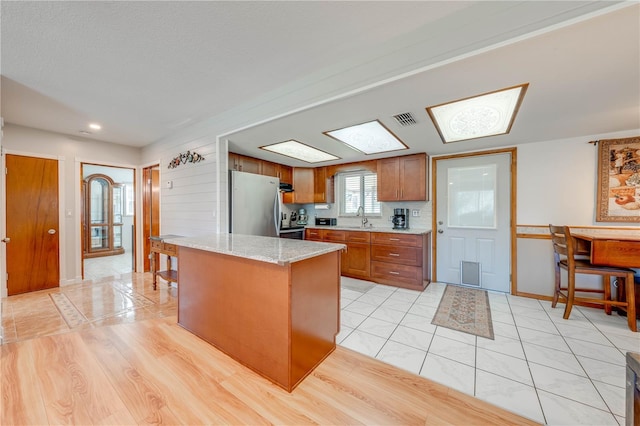 kitchen with light stone countertops, brown cabinetry, visible vents, freestanding refrigerator, and a sink