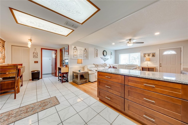 kitchen featuring light stone counters, visible vents, light tile patterned flooring, ceiling fan, and open floor plan