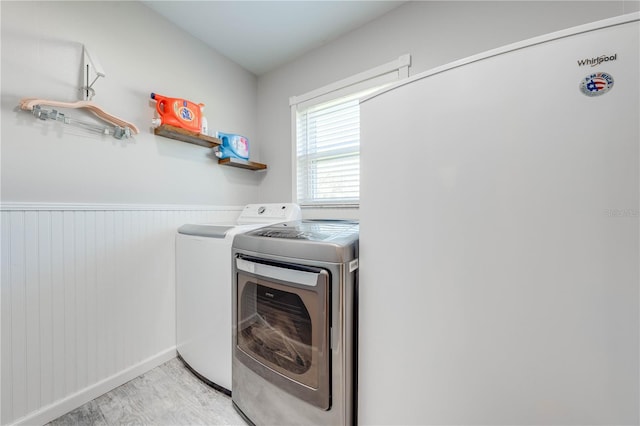 clothes washing area featuring light wood-type flooring, wainscoting, laundry area, and washing machine and clothes dryer