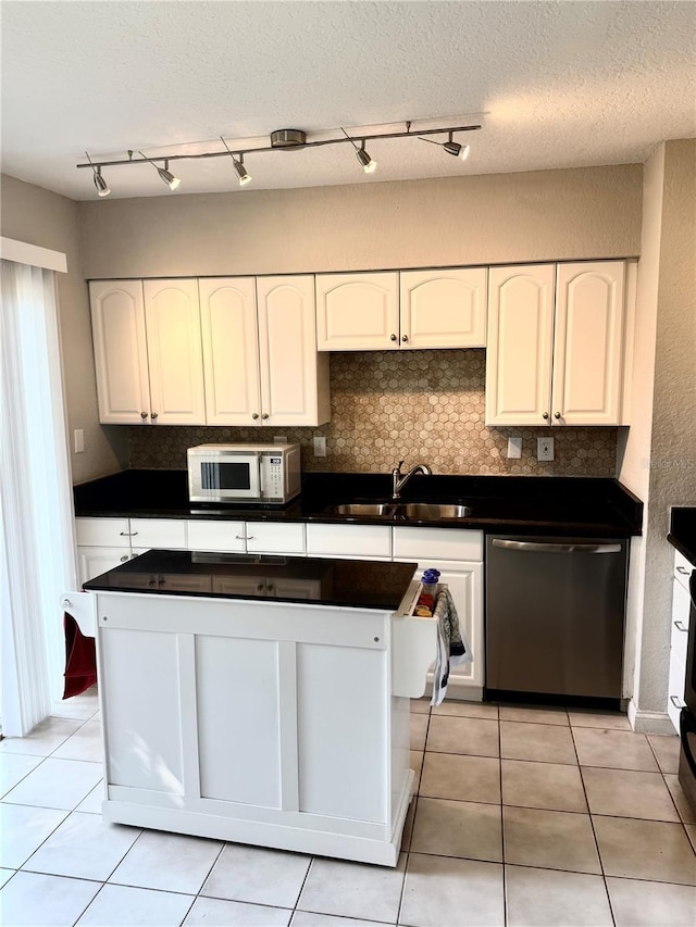 kitchen with white microwave, a sink, decorative backsplash, dishwasher, and dark countertops