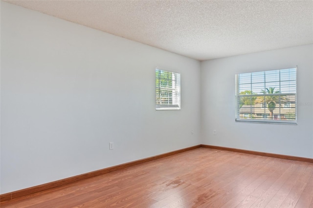 empty room featuring light wood-style floors, baseboards, and a textured ceiling