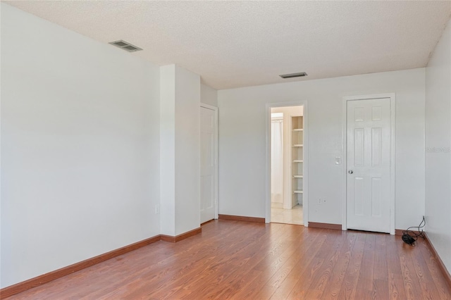 spare room with visible vents, baseboards, a textured ceiling, and hardwood / wood-style floors