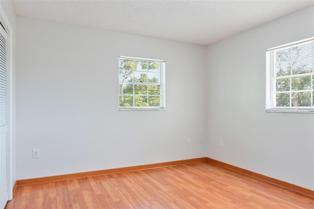 spare room with light wood-type flooring, baseboards, and a textured ceiling