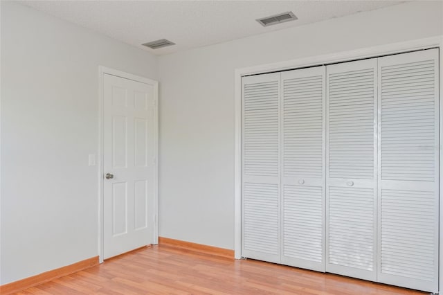 unfurnished bedroom with a closet, visible vents, baseboards, and light wood-style floors