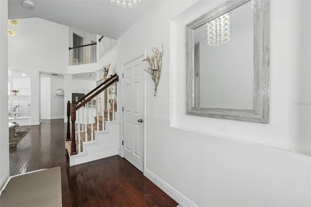 hallway featuring stairway, baseboards, an inviting chandelier, a towering ceiling, and wood-type flooring