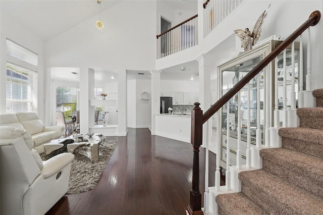 living area featuring dark wood finished floors, stairway, high vaulted ceiling, and ornate columns