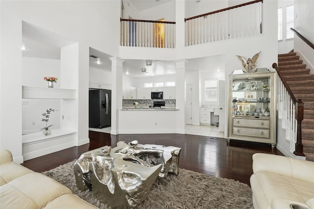 living room featuring stairway, wood finished floors, baseboards, ornate columns, and a towering ceiling